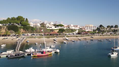 Aerial-dolly-sideways-along-Alvor-coastline,-Sailing-boats-by-the-pier-and-beach,-Algarve