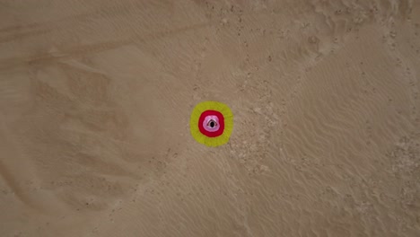 Woman-sits-on-sand-dune-in-colorful-bullseye-dress,-aerial-ascends