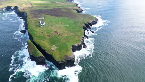 Rugged-coastline-with-waves-crashing-against-cliffs,-green-pastures-beside-the-ocean