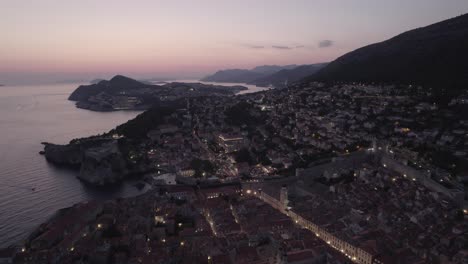 Toma-Aérea-De-Establecimiento-De-Dubrovnik-Después-Del-Atardecer,-Pintoresca-Ciudad-Costera,-Volando-Hacia-Atrás