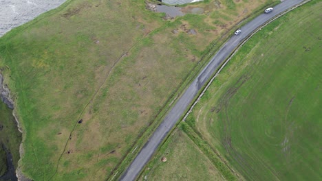 Curvy-road-amidst-green-fields-with-a-cliff-edge-nearby-from-drone-view