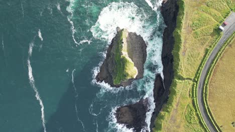 Aerial-view-of-a-rugged-coastline-with-waves-crashing-on-rocks,-greenery-nearby