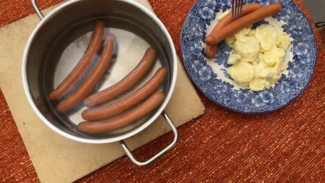 Putting-typical-German-bockwurst-sausage-on-a-plate-with-freshly-made-potato-salad-High-angle-view