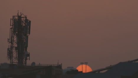 Timelapse-of-sun-setting-behind-residential-buildings-and-a-mobile-tower-during-evening-sunset-time-in-india