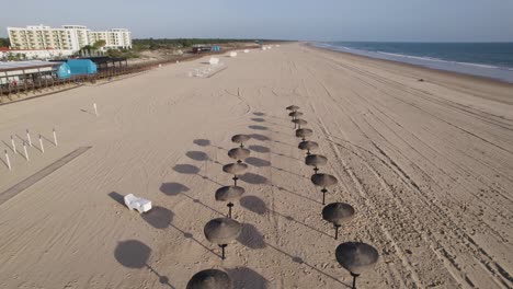 Drone-flying-backward-over-Montegordo-beach,-Sun-hats-from-beach-resort,-Algarve