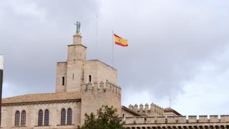 Bottom-up-shot-showing-spanish-flag-waving-in-wind-on-top-of-Cathedral-de-Mallorca-against-cloudy-sky