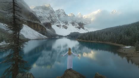 Lady-in-dress-slowly-raising-arms-in-front-of-magical-reflecting-lake-and-mountains