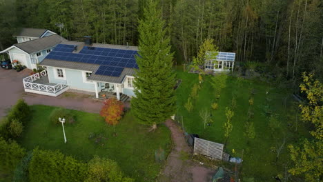 Aerial-view-behind-a-tree,-revealing-a-house-powered-by-solar-energy,-fall-day