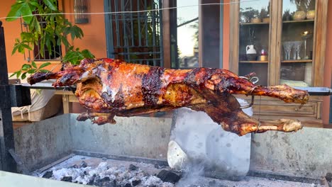 Roasting-whole-lamb-on-a-spit-metal-rotating-stick-over-fire,-golden-crispy-skin,-lamb-bbq-grill,-delicious-meat,-4K-shot