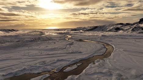 Aerial-landcsape-view-over-a-river-flowing-from-Sólheimajökull-glacier's-ice-melting,-climate-change,-in-Iceland,-during-sunset
