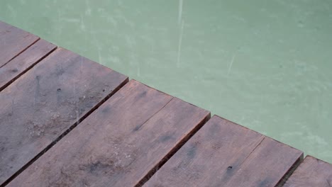 Nahaufnahme-Von-Holzplanken-Des-Kaipiers-Mit-Einem-Blick-Auf-Meerwasser-Und-Regentropfen,-Die-Bei-Schlechtem-Wettersturm-Und-Regenguss-An-Einem-Tropischen-Reiseziel-Fallen