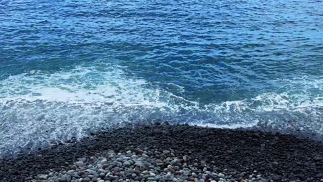 Blue-clean-ocean-water-washes-on-pebble-stone-beach-in-Tenerife-Spain