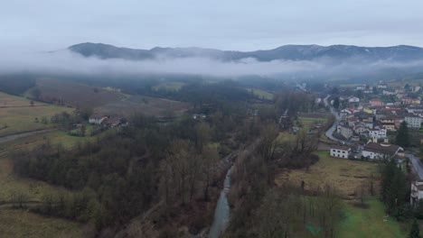 Mist-cloud-over-countryside-river-valley-with-village-and-overcast-sky