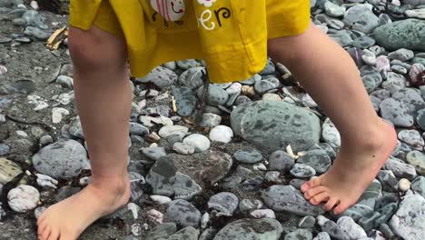 Girl-walking-barefoot-across-stones-on-beach