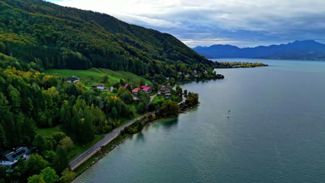 Luftaufnahme-Eines-Natürlichen-Sees,-Grüne-Hügel-Und-Uferstraße,-Bergiger-Blauer-Himmel