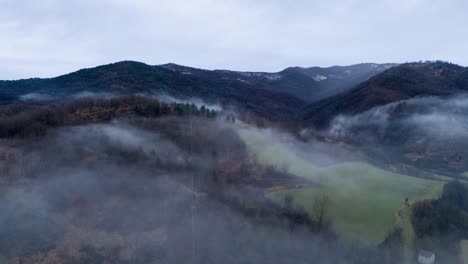 Mist-clouds-over-hilly-countryside-landscape-below-gray-sky,-timelapse