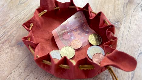Taking-money-and-euro-coins-out-of-a-small-handmade-leather-pouch-close-up