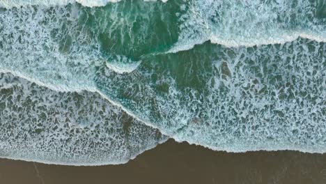 Foamy-Waves-Splashing-Sandy-Shore-Of-The-Beach---Aerial-Top-Down