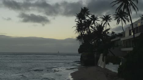 Das-Zwielicht-Der-Untergehenden-Sonne-Zeichnet-Die-Silhouetten-Der-Palmen-Auf-Einer-Halbinsel-Auf-Oahu,-Hawaii,-Während-Der-Pazifische-Ozean-Anmutig-An-Die-Küste-Rollt