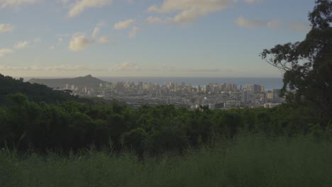 Mountain-top-view-of-the-city-of-Honolulu,-Hawaii-as-the-setting-sun-reflects-pink-hues-onto-the-clouds,-The-blue-Pacific-water-graces-the-horizon