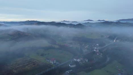 Mist-hovering-over-hilly-village-countryside-landscape-at-dawn,-Italy