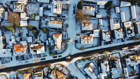 Top-down-aerial-of-a-car-driving-slowly-over-a-frozen-route-in-a-suburban-neighborhood-on-a-sunny-winter-day