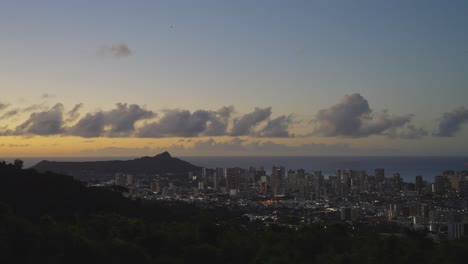 La-Ciudad-De-Honolulu-Al-Atardecer-Desde-Una-Vista-De-Una-Montaña-Mientras-El-Sol-Refleja-Un-Brillo-Anaranjado-En-El-Cielo.