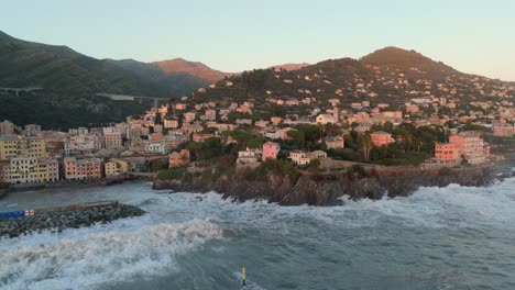 Large-sea-waves-breaking-on-rocky-harbor-coast-with-houses,-Genoa-city