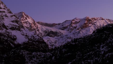 Pink-light-at-sunset-on-snowy-mountains-with-dam-in-foreground,-Valmalenco-in-Italy