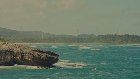 Die-Küste-Von-Oahu-Säumt-Den-Horizont,-Während-Das-Weiße,-Türkisfarbene-Wasser-Des-Pazifischen-Ozeans-Gegen-Die-Von-Felsbrocken-Gesäumte-Küste-Im-Osten-Von-Honolulu,-Hawaii,-Rollt,-Während-Windturbinen-Energie-Aus-Dem-Wind-Gewinnen