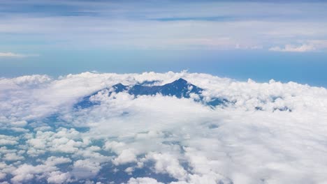 Vista-Aérea-De-La-Cima-De-Una-Montaña-Volcánica-Escarpada-Y-Rocosa-Que-Alcanza-Su-Punto-Máximo-A-Través-De-Espesas-Nubes-En-Indonesia