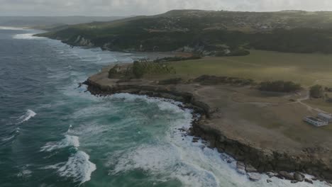 Panoramic-aerial-parallax-above-powerful-ocean-waves-crashing-on-jagged-shoreline-of-Cove-Bay-St-Lucy-Barbados-at-sunset