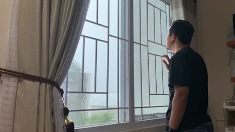 Pensive-sad-asian-man-stands-at-the-window