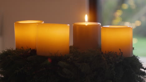 Three-glowing-candles-on-evergreen-wreath,-festive-ambiance