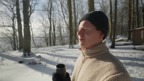 Sunlit-winter-moment-as-a-person-sips-from-a-thermos,-enjoying-a-hot-beverage-in-a-snowy-forest