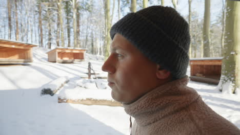Nahaufnahme-Eines-Mannes-In-Winterkleidung,-Der-Aus-Einer-Thermosflasche-In-Einem-Verschneiten-Wald-Mit-Holzhütten-Im-Hintergrund-Trinkt