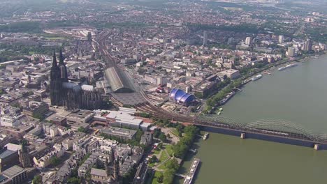 Cologne-cityscape-with-iconic-Cathedral-and-Rhine-River-and-a-train-entering,-daytime,-aerial-view
