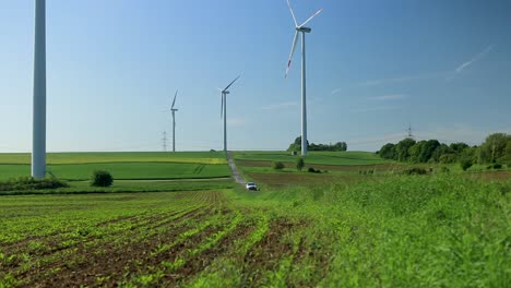 Wind-turbines-towering-over-green-fields-with-a-clear-blue-sky,-a-road-slicing-through-the-landscape