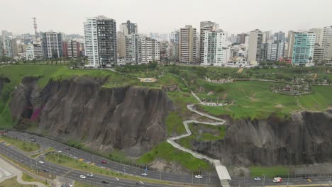 From-urban-heights-to-coastal-beauty:-Drone-unveils-Miraflores'-buildings,-widens-to-reveal-the-highway-and-ocean-waves
