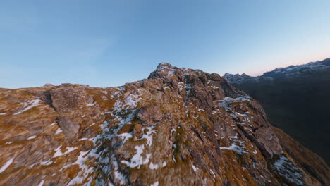 Reveal-of-the-snowy-mountain-range-in-Lofoten-Islands-in-Norway,-impressive-cinematic-FPV-drone-close-flight