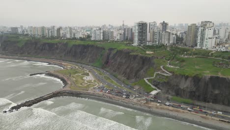 Panoramic-splendor-in-Miraflores:-Drone-captures-the-synergy-of-ocean-waves,-coastal-highway,-and-urban-skyline