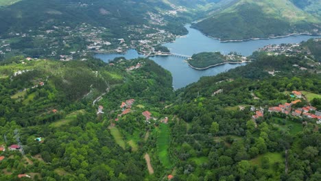 Aerial-View-of-Houses-in-Peneda-Gerês-National-Park,-Portugal,-with-Caniçada-Dam-in-the-Sunny-Day-Background