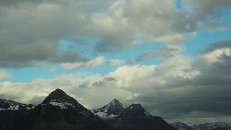 Mountain-peaks-with-snow-under-a-dramatic-cloudy-sky-from-a-moving-car's-perspective