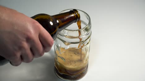 Ein-Dunkles-Bier-Mit-Einer-Dicken-Schaumschicht-In-Ein-Pintglas-Auf-Einer-Weißen-Tischplatte-Gießen
