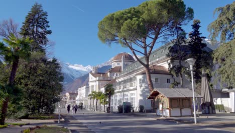 People-are-walking-along-the-Kurpromenade-in-front-of-the-Kurhaus-in-Meran---Merano,-South-Tyrol,-Italy-on-a-sunny-winter`s-day