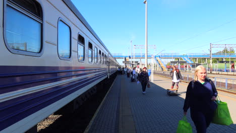 People-walking-with-suitcases-next-to-Ukrainian-Railways-Ukrzaliznycia-train-at-the-Chelm-train-station-in-Poland,-people-traveling,-sunny-weather,-4K-shot