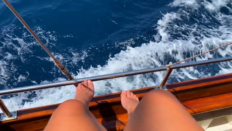 Female-legs-and-feet-on-a-wooden-sailing-boat-and-sea-waves,-fun-summer-vacation,-moving-boat,-sunny-holiday,-4K-shot