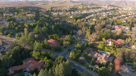 Flying-Over-Upscale-Neighborhood-of-Calabasas,-California-at-Sunset-with-Mountains-on-Horizon-and-Car-Driving-Below