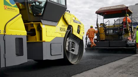 Construction-workers-in-high-visibility-clothing-operating-paving-machinery-on-a-new-road,-cloudy-day-near-Buenos-Aires