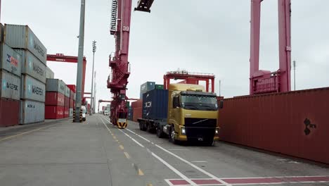LKW,-Der-Tagsüber-Durch-Einen-Belebten-Containerterminal-Fährt,-Mit-Kränen-Und-Gestapelten-Schiffscontainern-Im-Hafen-Von-Buenos-Aires